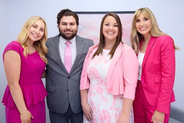 Four smiling professionals in business attire pose for a portrait together.