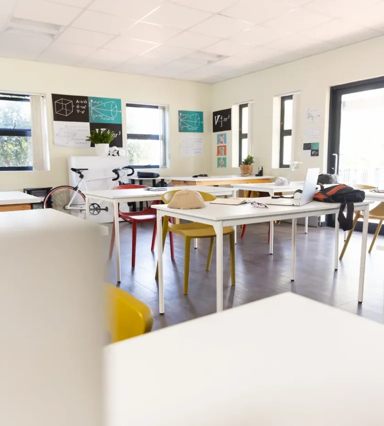 A bicycle sits on a white table in a bright classroom with math equations displayed on the walls.